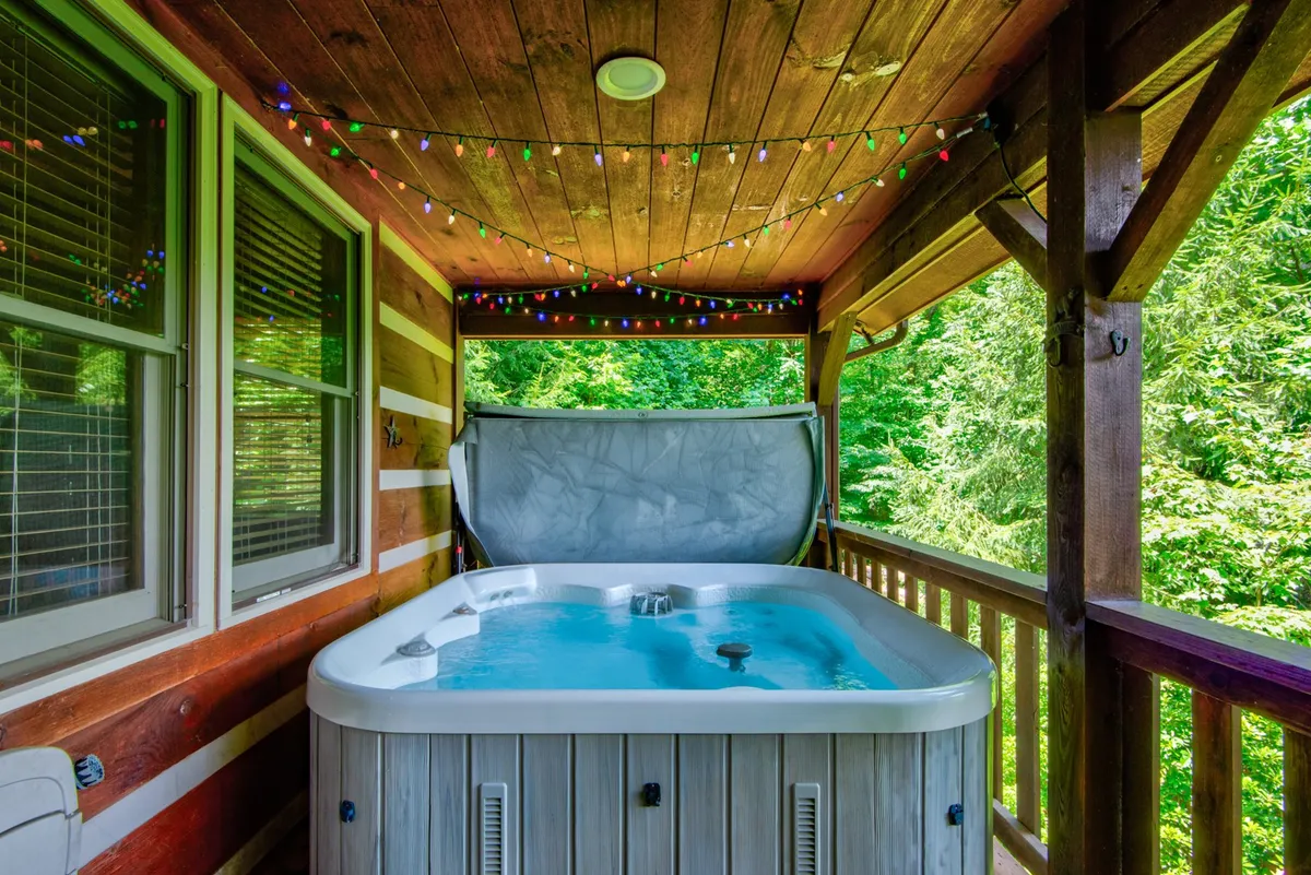 A cozy outdoor hot tub beneath string lights, surrounded by greenery and a wooden structure. The mood is tranquil, perfect for evening relaxation.