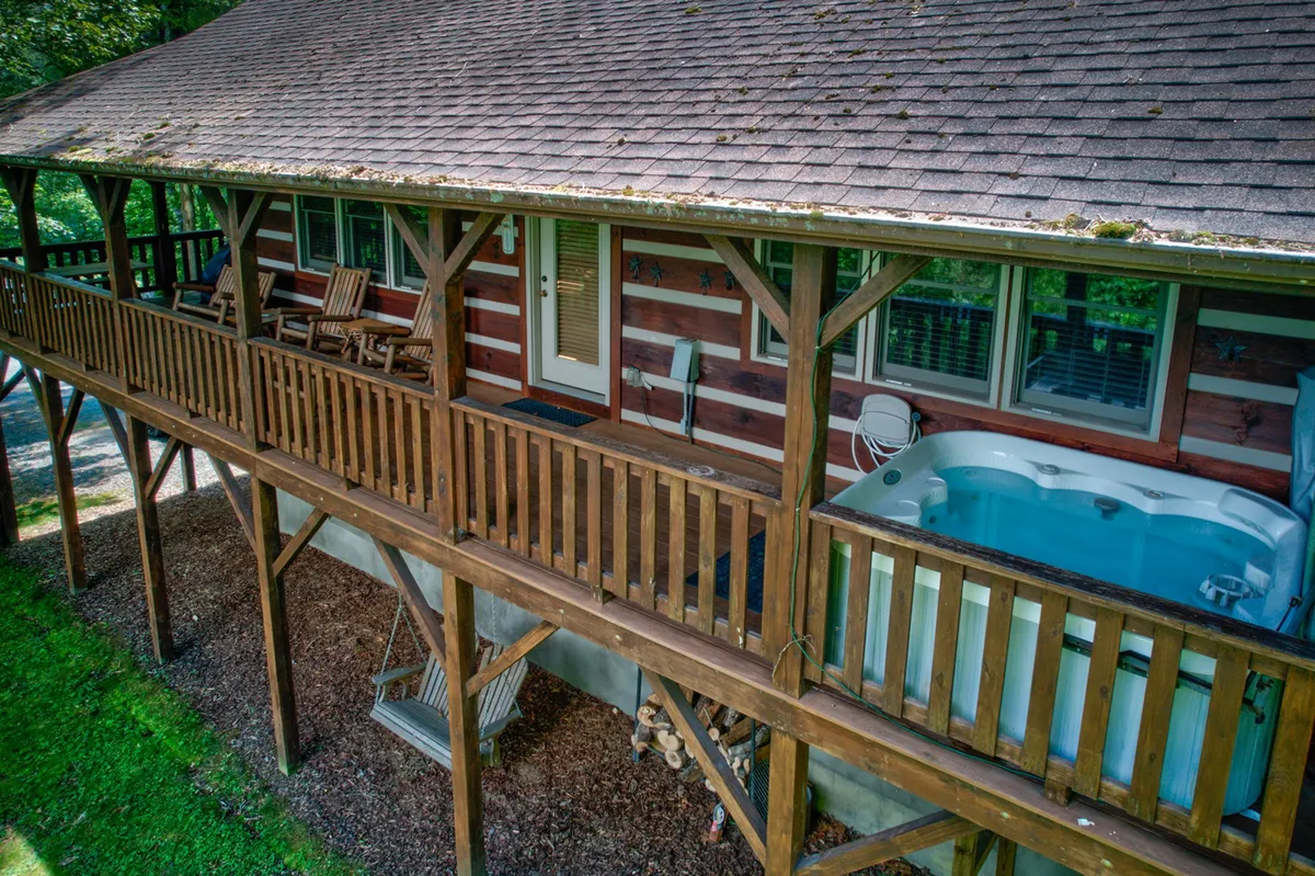 A spacious wooden deck with a bubbling spa/hot tub and inviting rocking chairs, framed by natural log siding. The scene is cozy and relaxed, with hints of nature seen just beyond the deck.