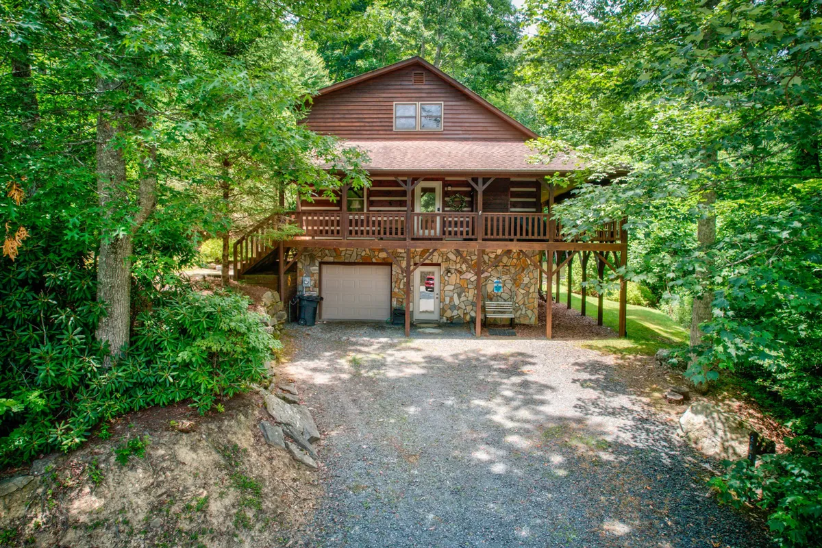 The hero image showcases the exterior of a charming wooden cabin with a stone facade, nestled amidst lush greenery. A welcoming front porch invites guests to relax, while the surrounding landscape hints at mountain views and serene natural beauty. The cabin exudes a cozy, inviting mood, perfect for gatherings, relaxation, and outdoor activities.