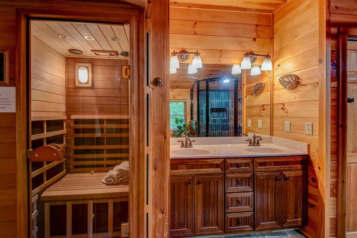 A tranquil spa-like bathroom featuring a double sink vanity, a wooden sauna, warm wood paneling, and decorative mirrors. The sauna is an inviting highlight, and the space feels both luxurious and relaxing—ideal for unwinding after mountain adventures.