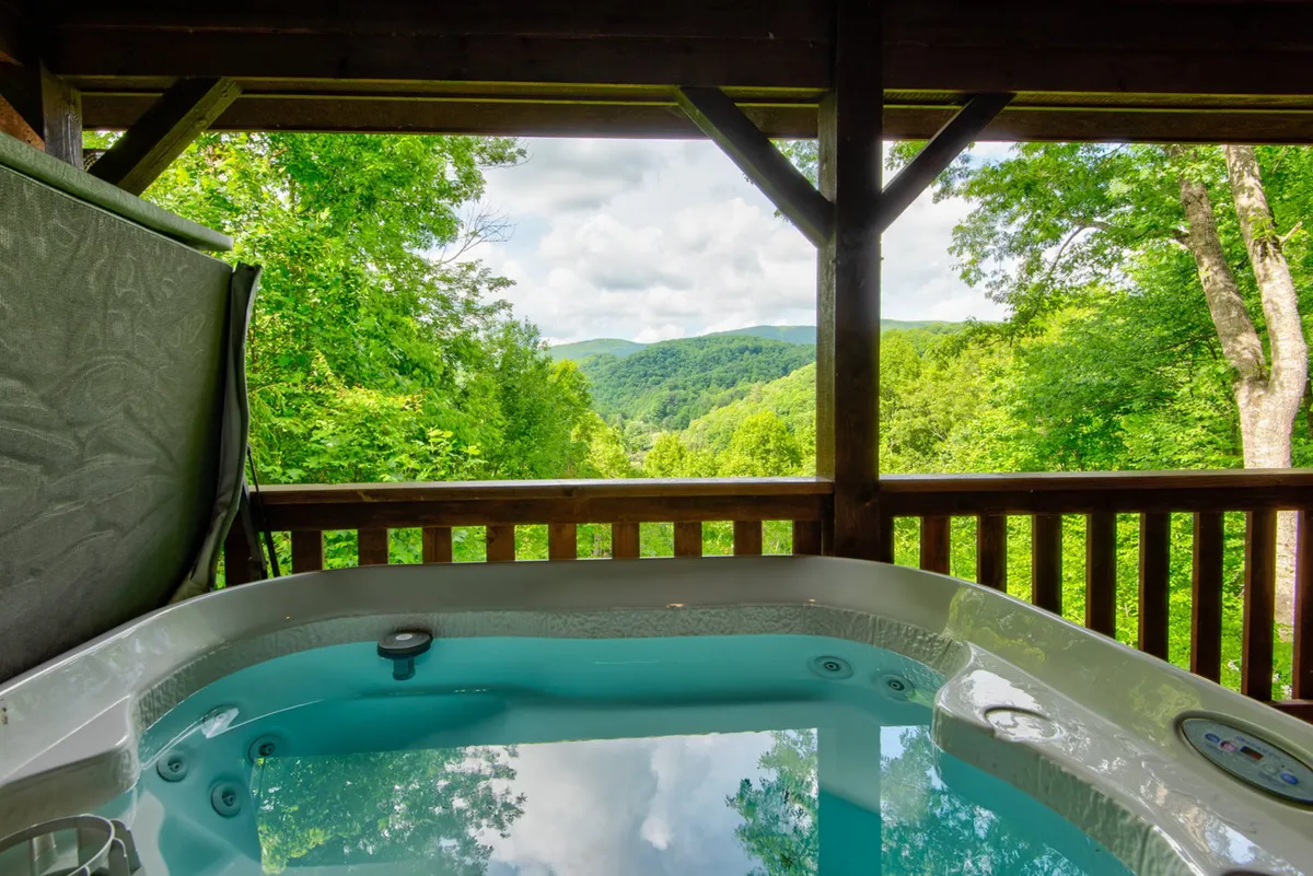 This image features an inviting hot tub on a wooden deck, with a sweeping mountain view framed by a sturdy wooden railing. The tranquil scene is enhanced by the presence of friends or family relaxing in the tub, basking in the sunset glow, and enjoying the natural beauty around them.